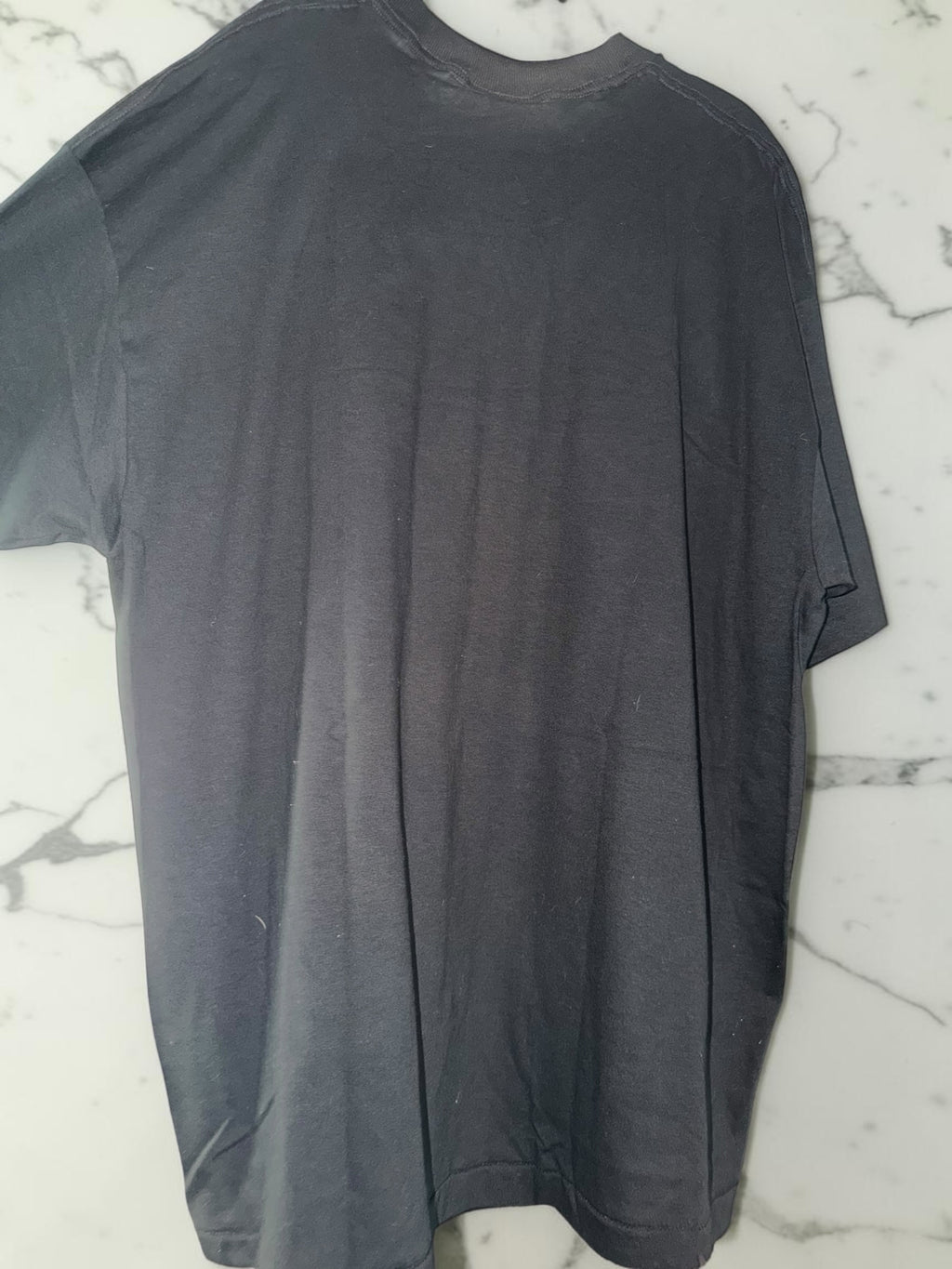 DRIPPING IN VINTY black cotton t-shirt with a plain back view, hanging against a white marble background.